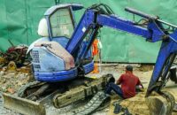 En blå Takeuchi minigrävare under reparation på en byggarbetsplats i staden.