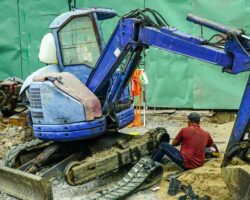 En blå Takeuchi minigrävare under reparation på en byggarbetsplats i staden.