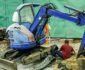 En blå Takeuchi minigrävare under reparation på en byggarbetsplats i staden.