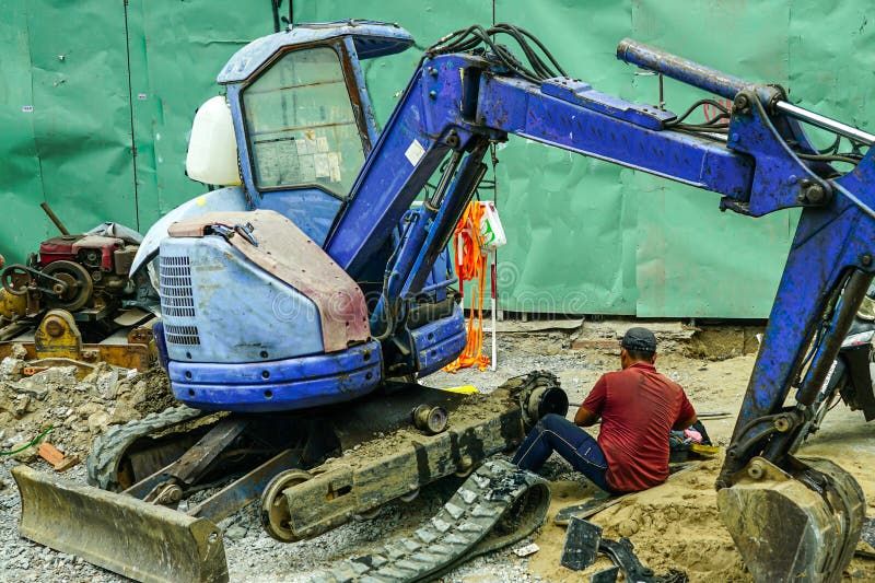 En blå Takeuchi minigrävare under reparation på en byggarbetsplats i staden.